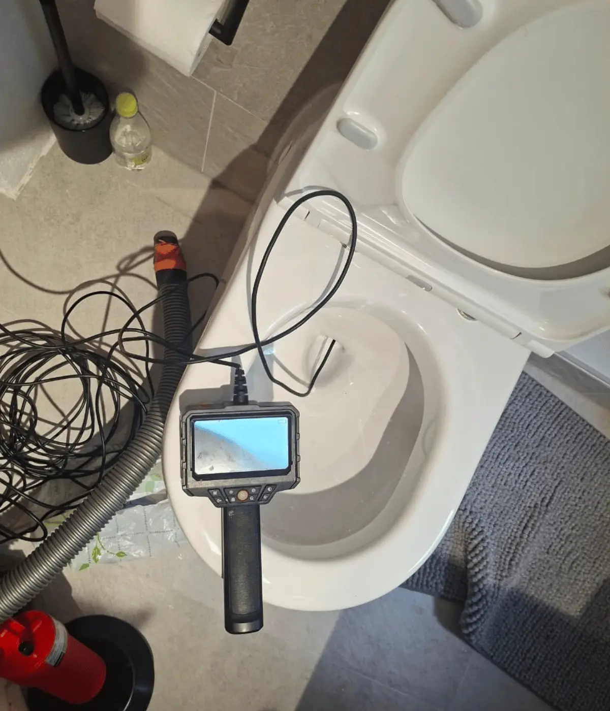 Caméra d'inspection et furet préparés devant une cuvette de WC bouchée.